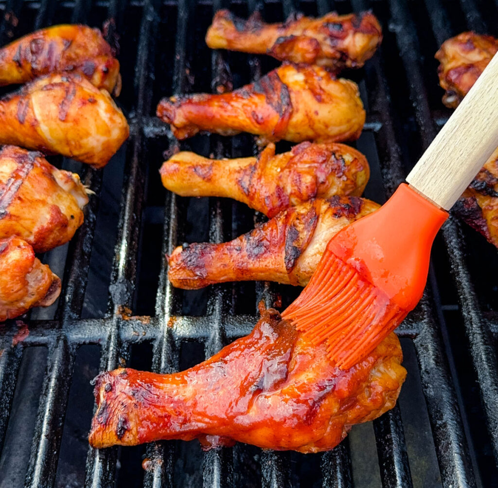 chicken drumsticks on a grill brushed with BBQ sauce