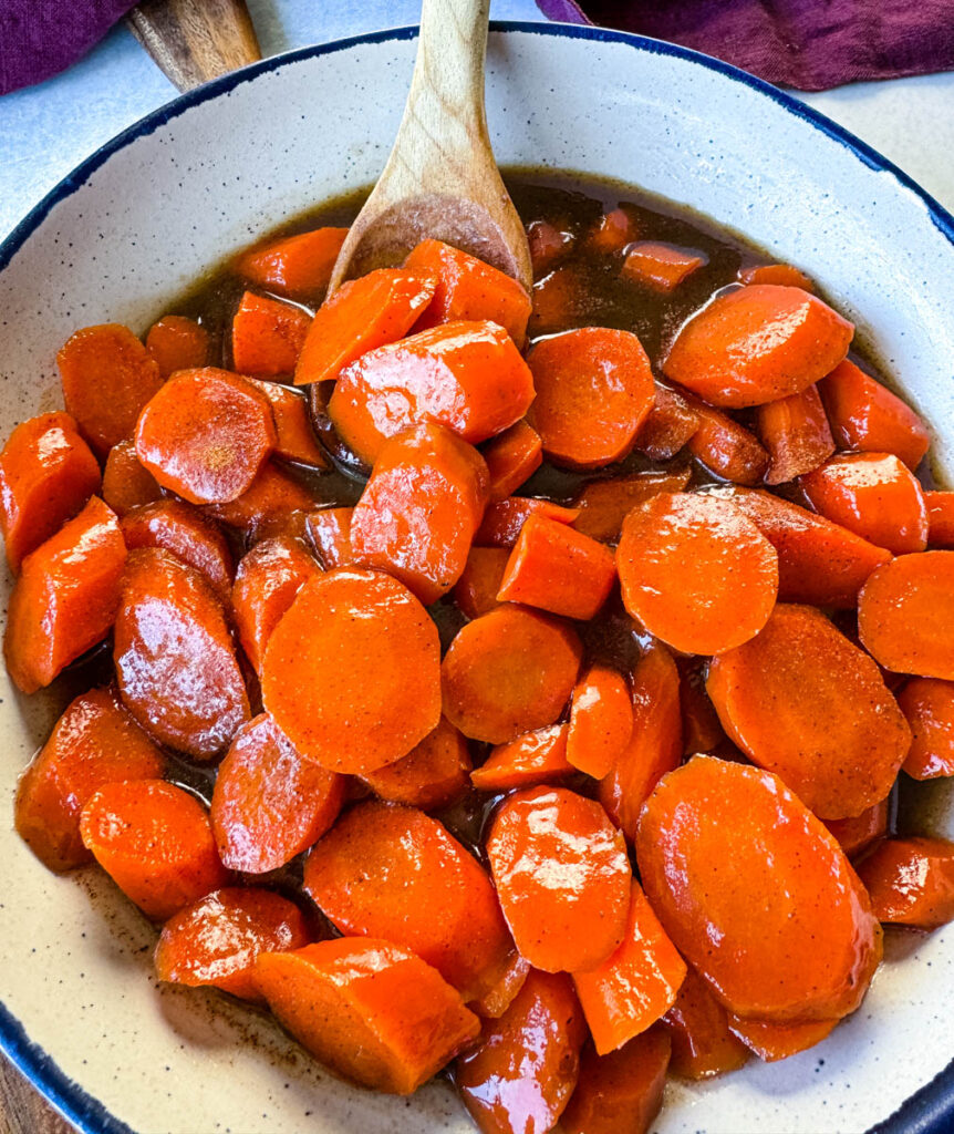 candied carrots with brown sugar cinnamon glaze in a white bowl with a wooden spoon