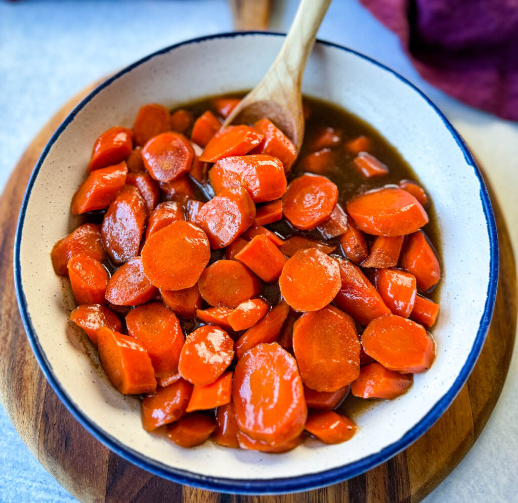 candied carrots with brown sugar cinnamon glaze in a white bowl with a wooden spoon