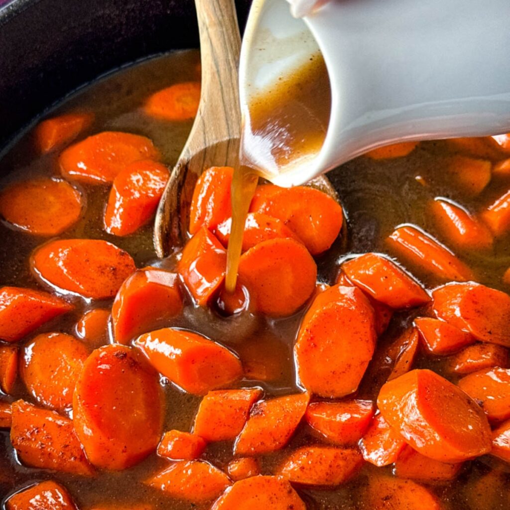 glaze poured over candied carrots with brown sugar cinnamon glaze in a cast iron skillet