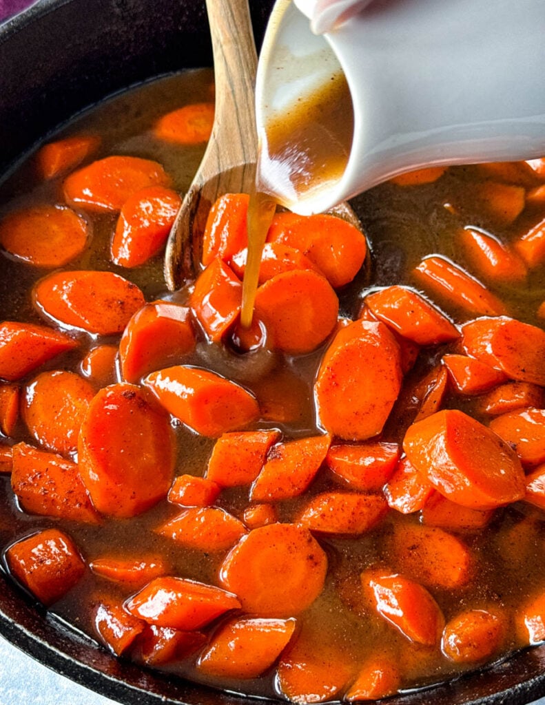 glaze poured over candied carrots with brown sugar cinnamon glaze in a cast iron skillet