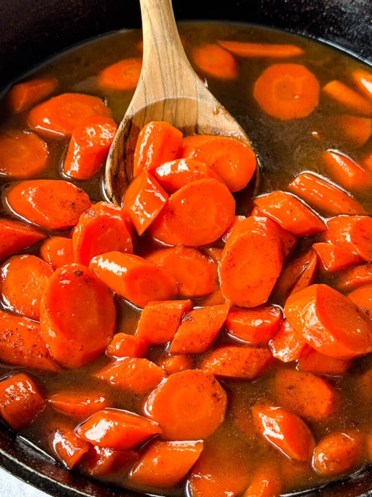 candied carrots with brown sugar cinnamon glaze in a cast iron skillet with a wooden spoon