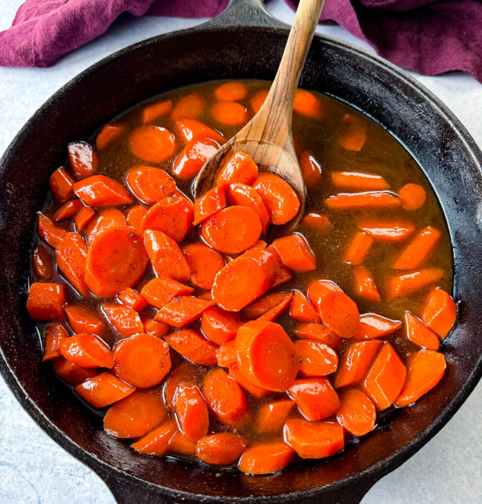 candied carrots with brown sugar cinnamon glaze in a cast iron skillet with a wooden spoon