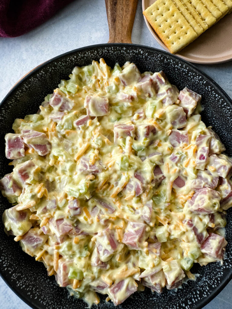ham salad with cheese in a black bowl with crackers