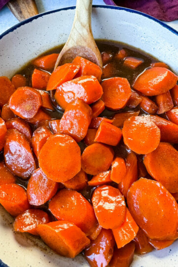 candied carrots with brown sugar cinnamon glaze in a white bowl with a wooden spoon