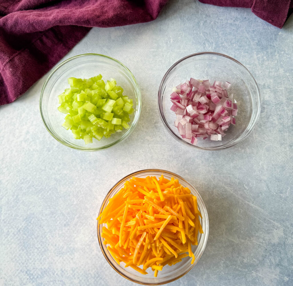 grated cheddar cheese, diced onions, and diced celery in separate glass bowls