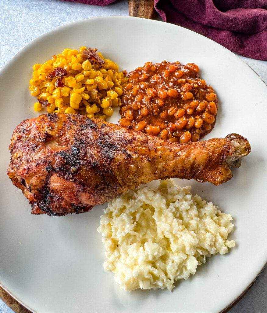 grilled turkey legs on a plate with baked beans, coleslaw, and fried corn