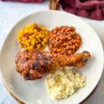 grilled turkey legs on a plate with baked beans, coleslaw, and fried corn