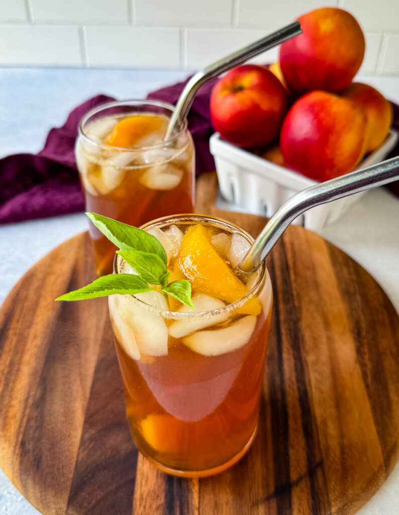 homemade peach tea in a glass with basil, peaches, and a straw