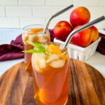 homemade peach tea in a glass with basil, peaches, and a straw