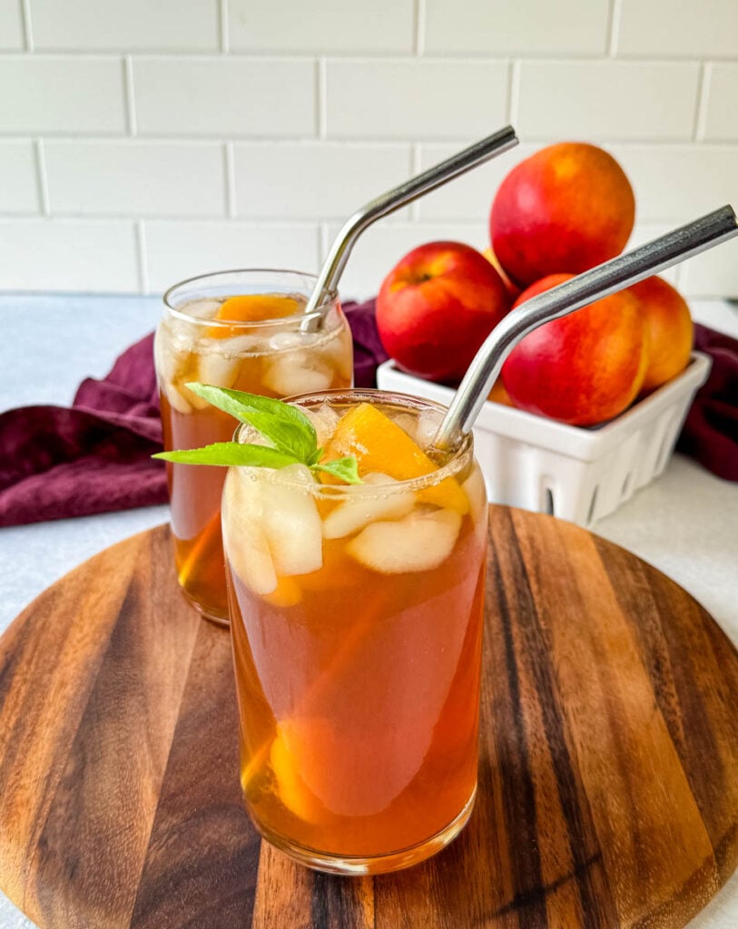 homemade peach tea in a glass with basil, peaches, and a straw