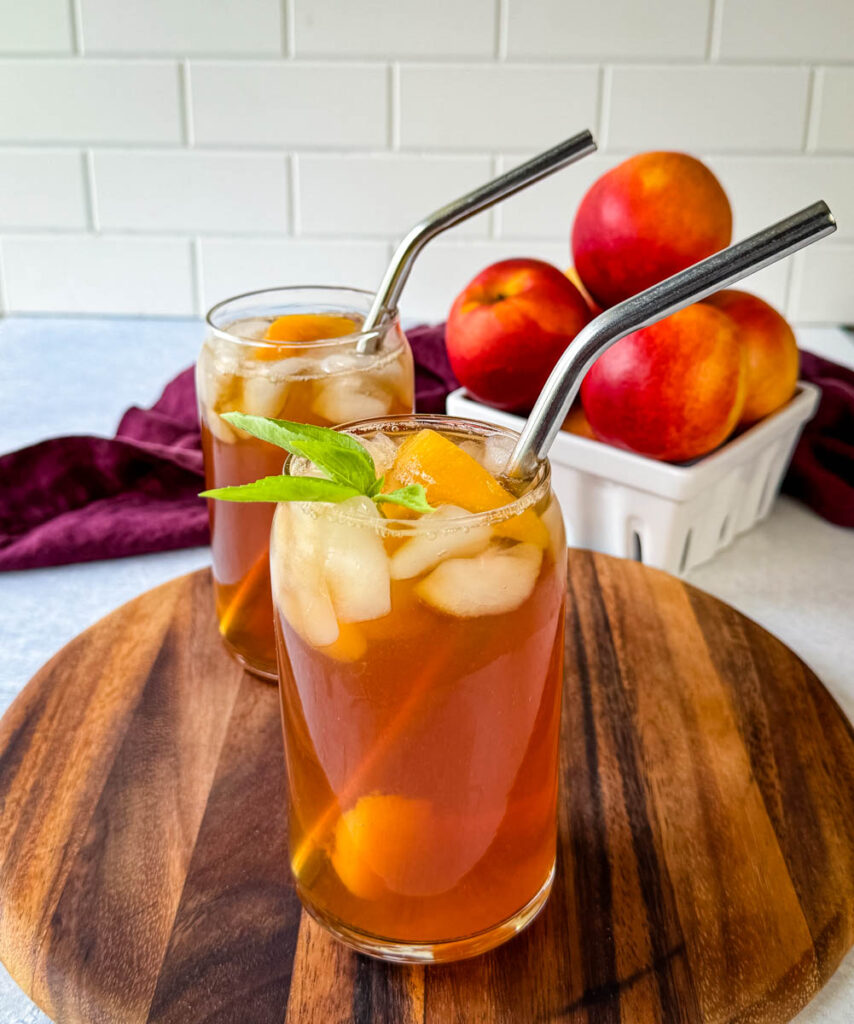 homemade peach tea in a glass with basil, peaches, and a straw