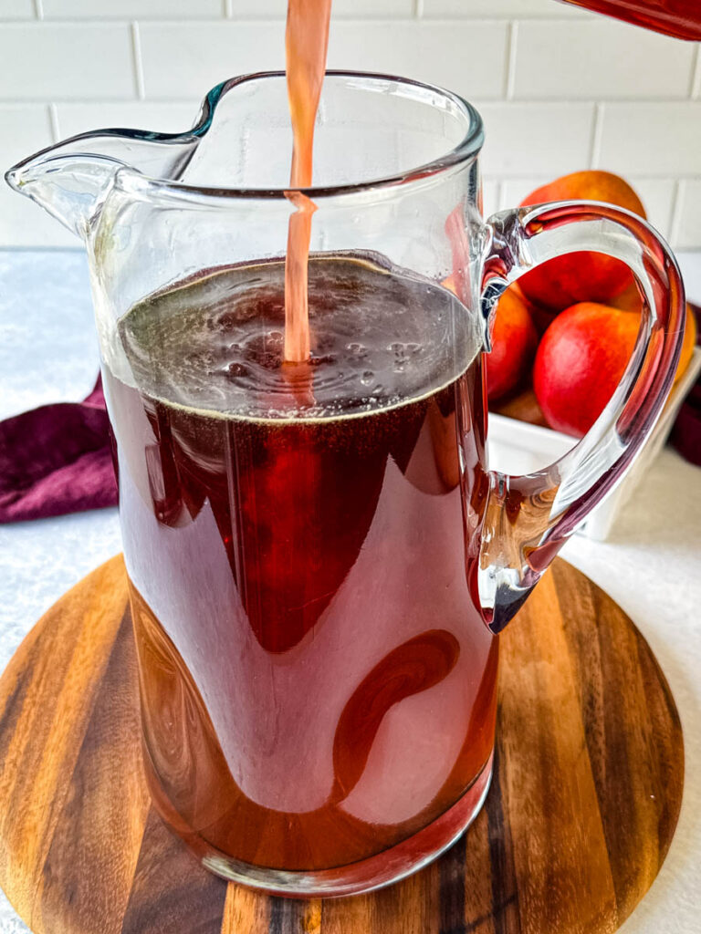 peach simple syrup poured in a pitcher of iced tea