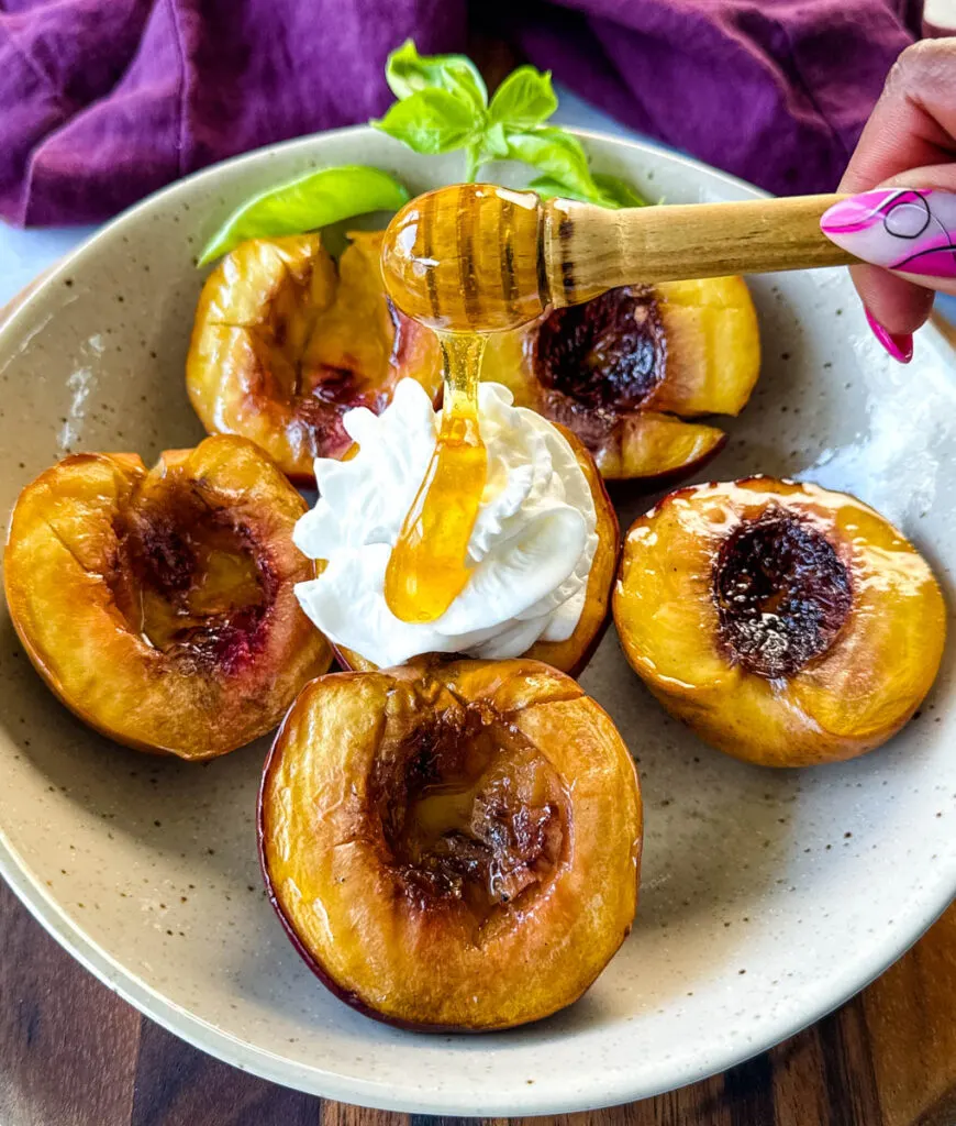 smoked peaches in a tan bowl with whipped cream and drizzled with honey