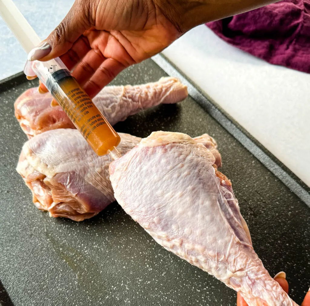 person injecting raw turkey leg with butter