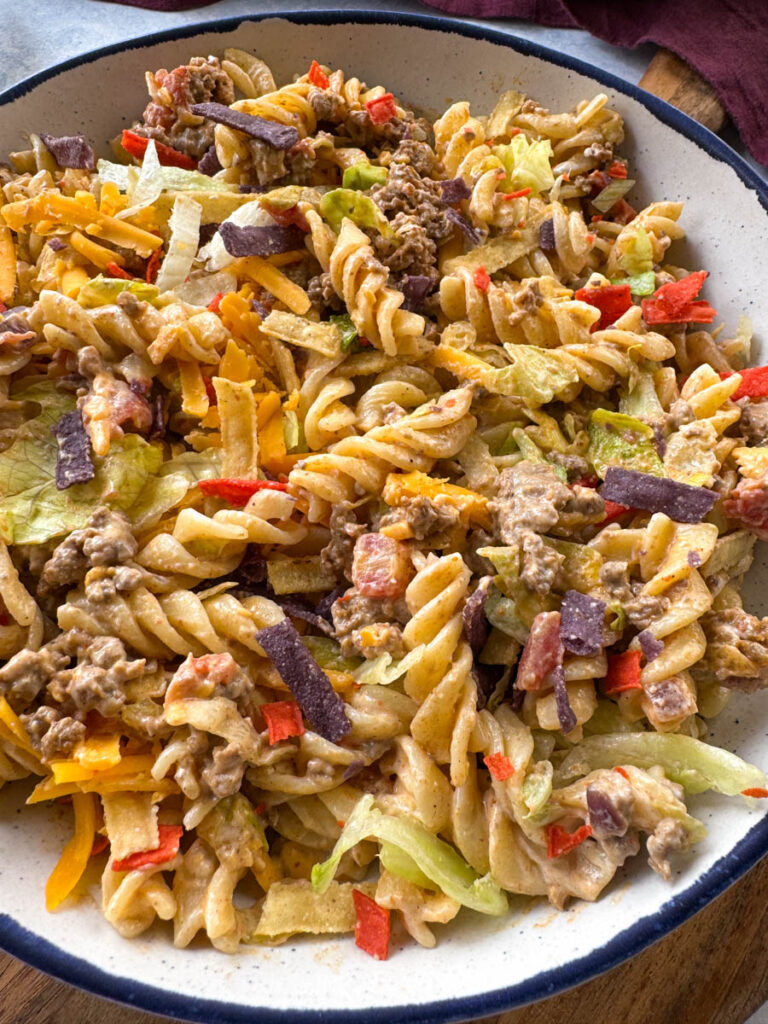 taco pasta salad with chips, cheese, and lettuce, in a white bowl