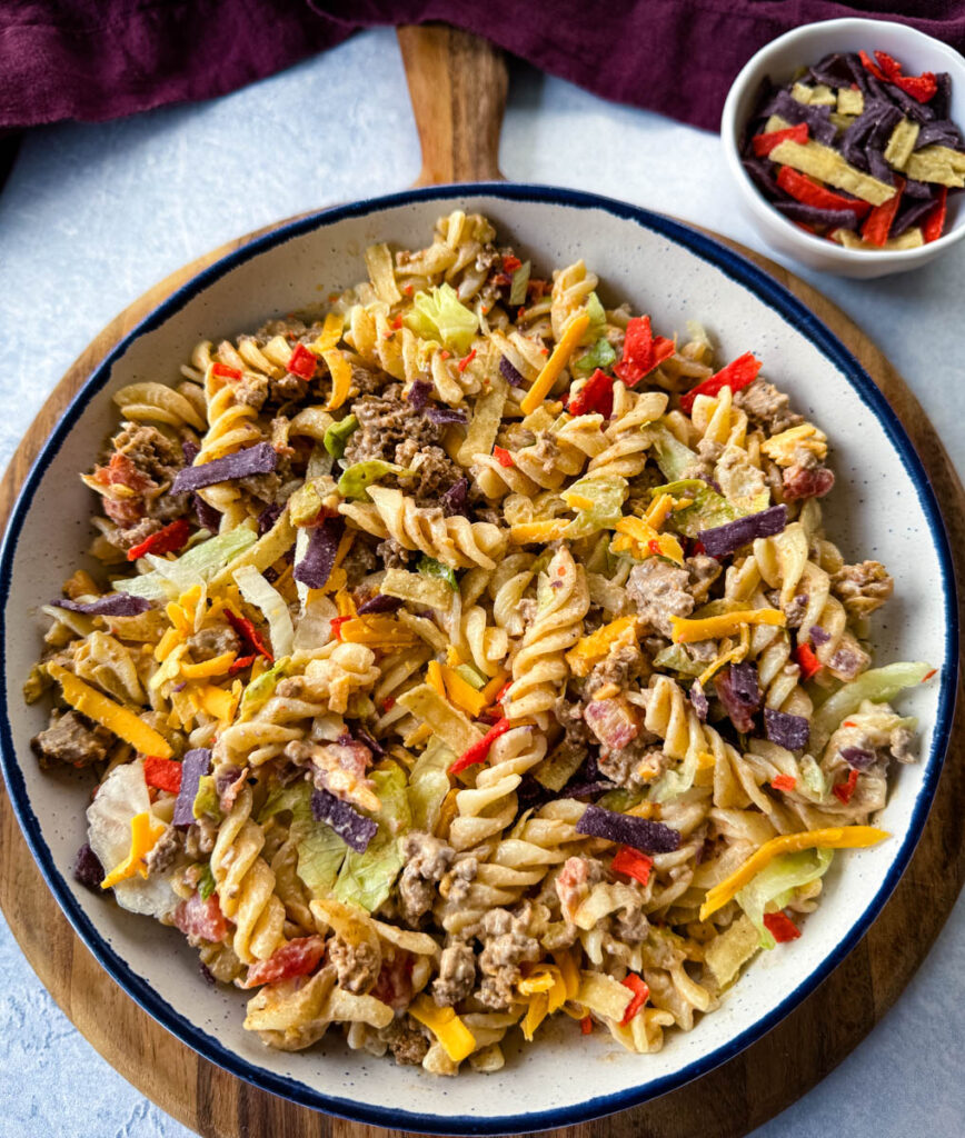 taco pasta salad with chips, cheese, and lettuce, in a white bowl