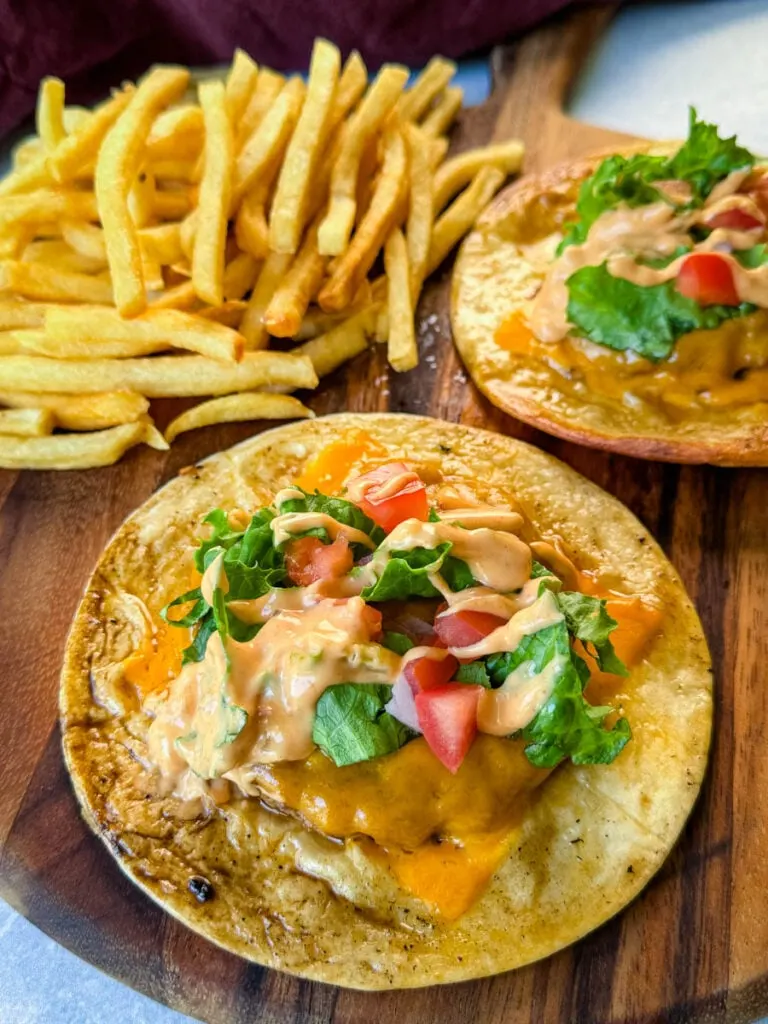 cheeseburger tacos with tomatoes, lettuce, and burger sauce on a plate with fries