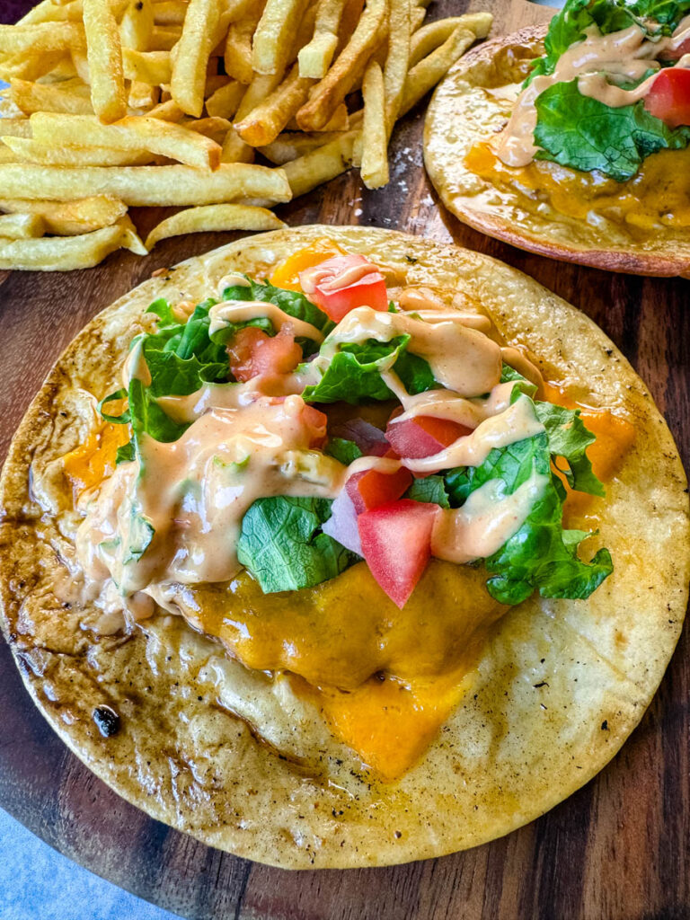 cheeseburger tacos with tomatoes, lettuce, and burger sauce on a plate with fries