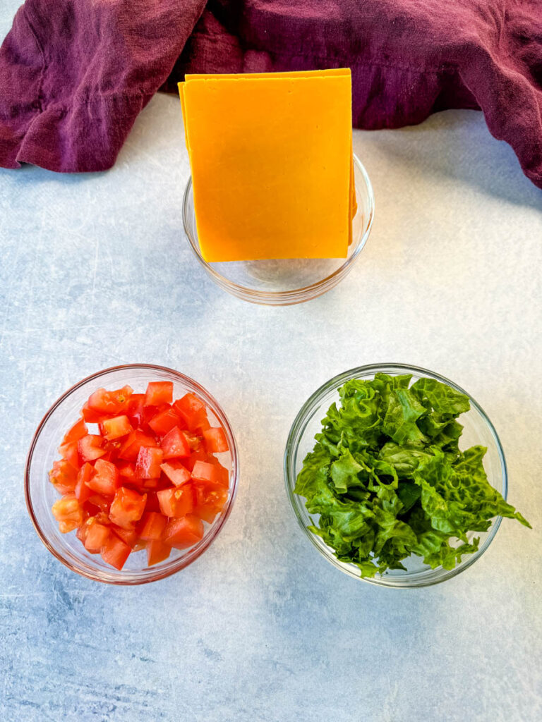 diced tomatoes, chopped lettuce, and slices of cheese in separate glass bowls