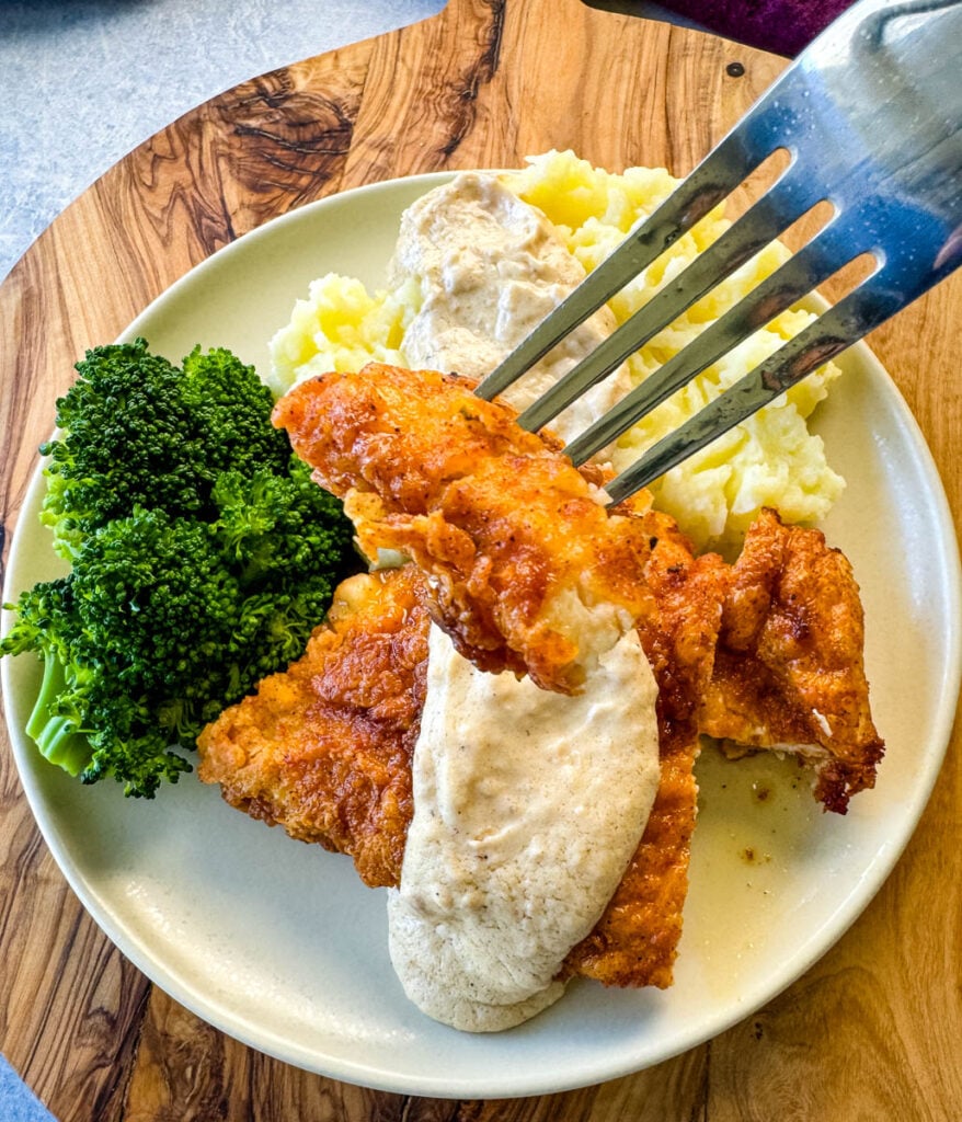 a piece of chicken fried chicken with gravy held by a fork