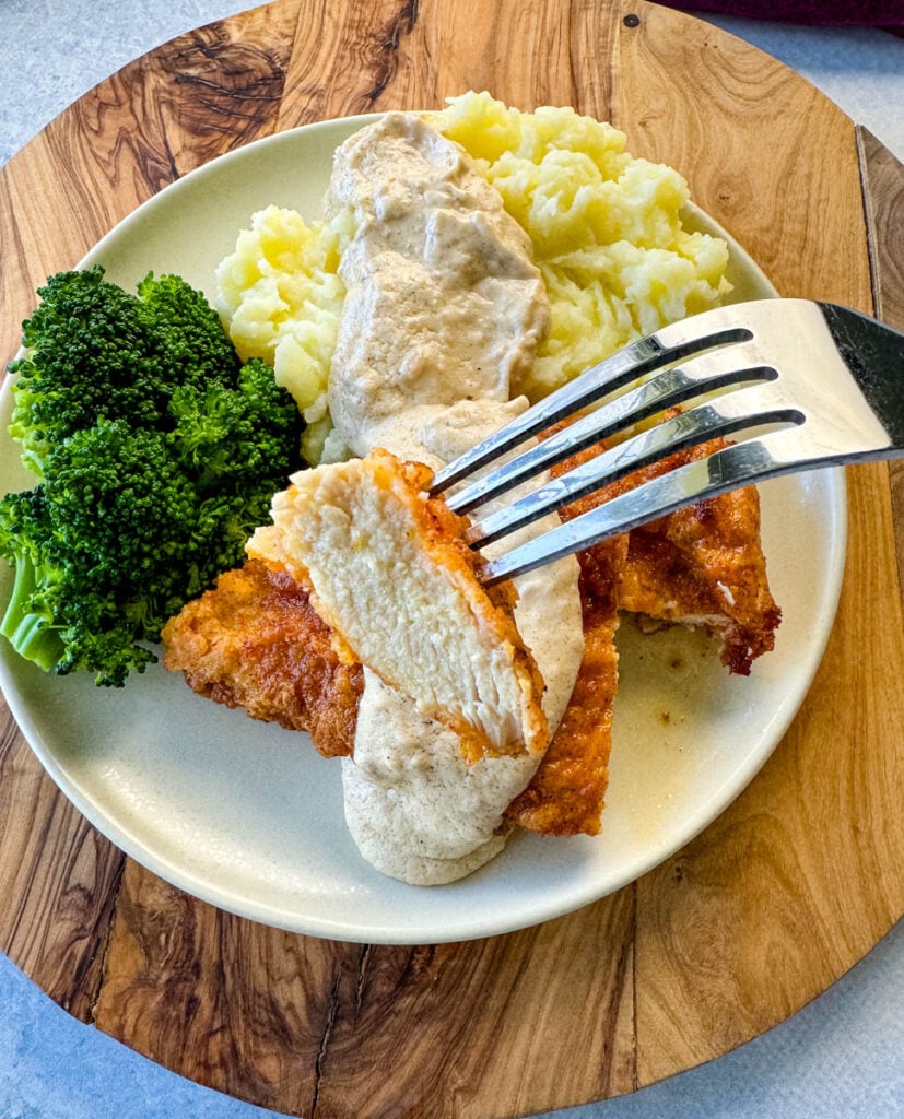 a piece of chicken fried chicken with gravy held by a fork