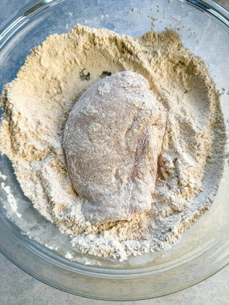 raw chicken coated in seasoned flour in a glass bowl