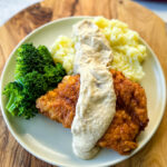 chicken fried chicken with gravy, mashed potatoes, and broccoli on a plate