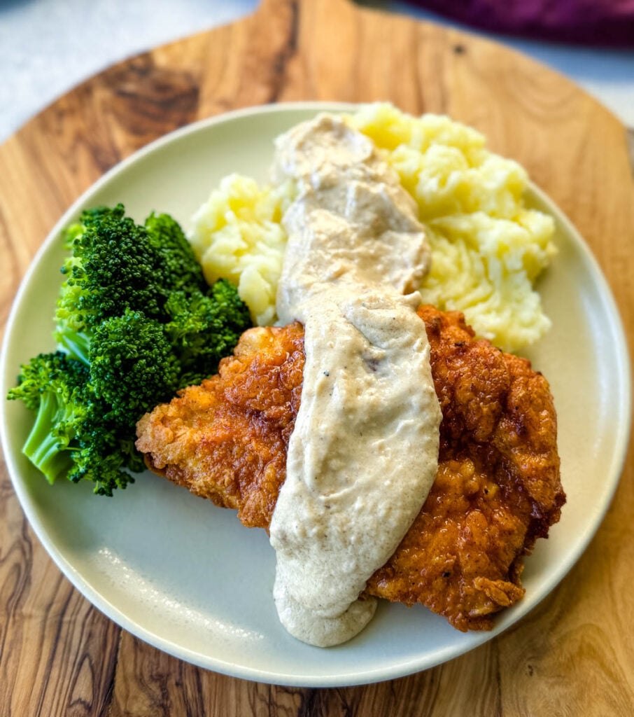 chicken fried chicken with gravy, mashed potatoes, and broccoli on a plate