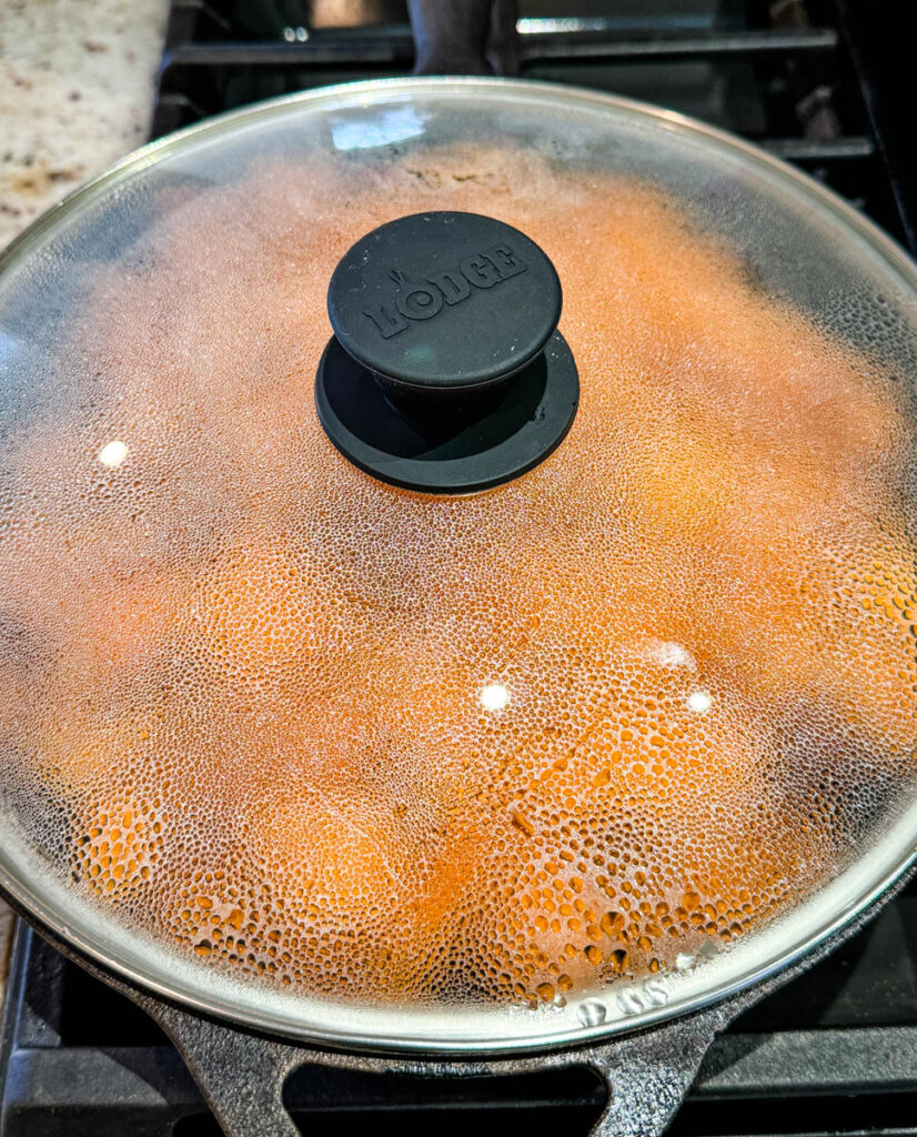 fried sweet potatoes in a cast iron skillet covered with a lid