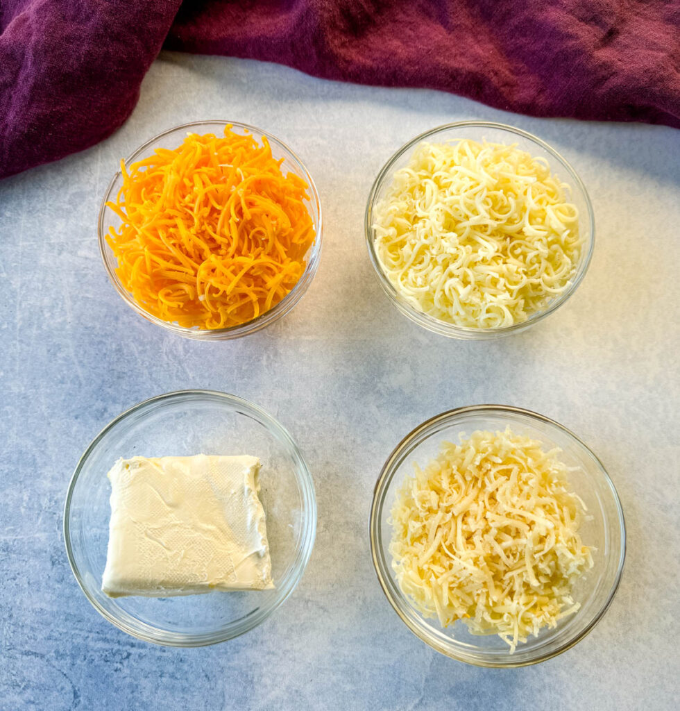 grated cheddar cheese, grated, mozzarella cheese, grated Parmesan cheese, and cream cheese in separate glass bowls