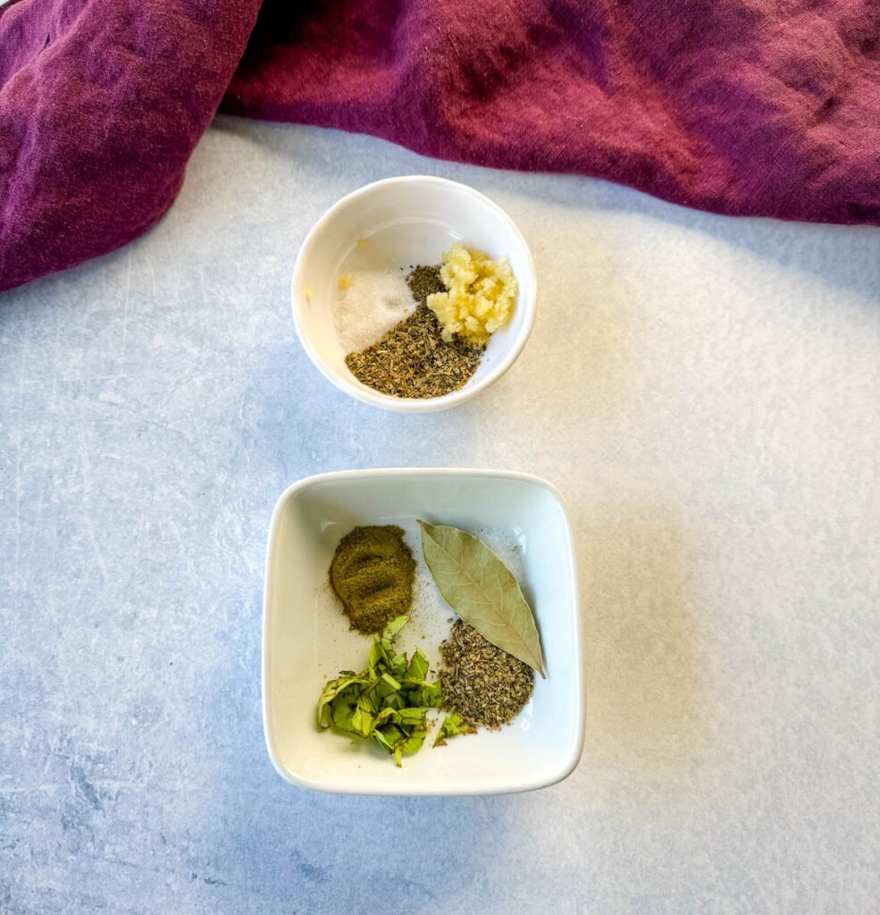 garlic, Italian seasoning, basil, bay leaf, salt and pepper in separate white bowls