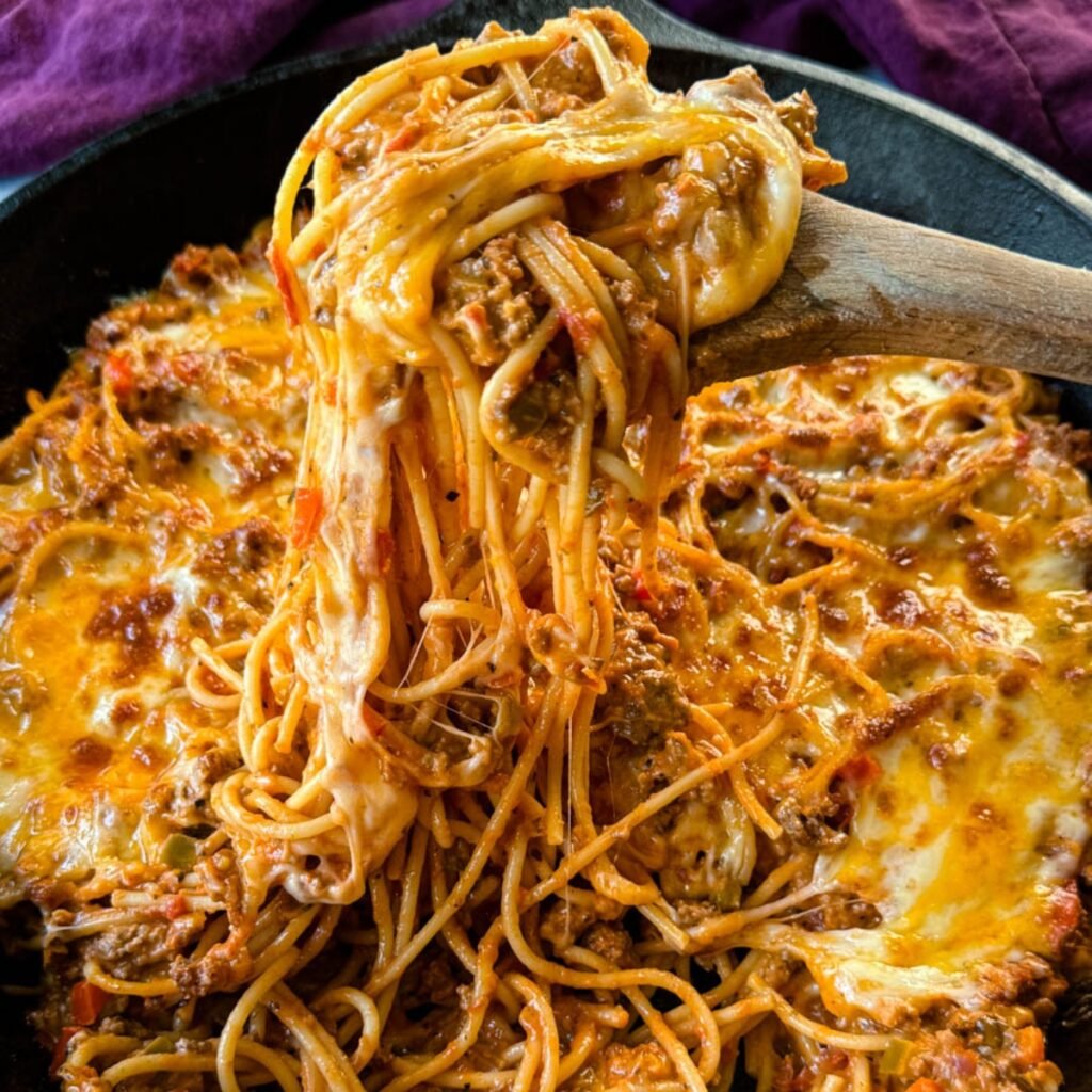 million dollar spaghetti in a cast iron skillet with a wooden spoon