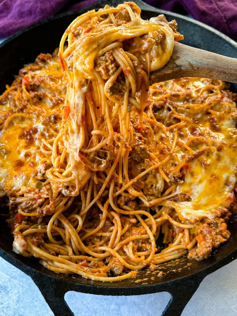 million dollar spaghetti in a cast iron skillet with a wooden spoon