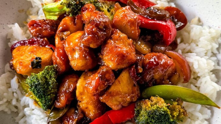 orange chicken with stir fry vegetables and white rice in a white bowl