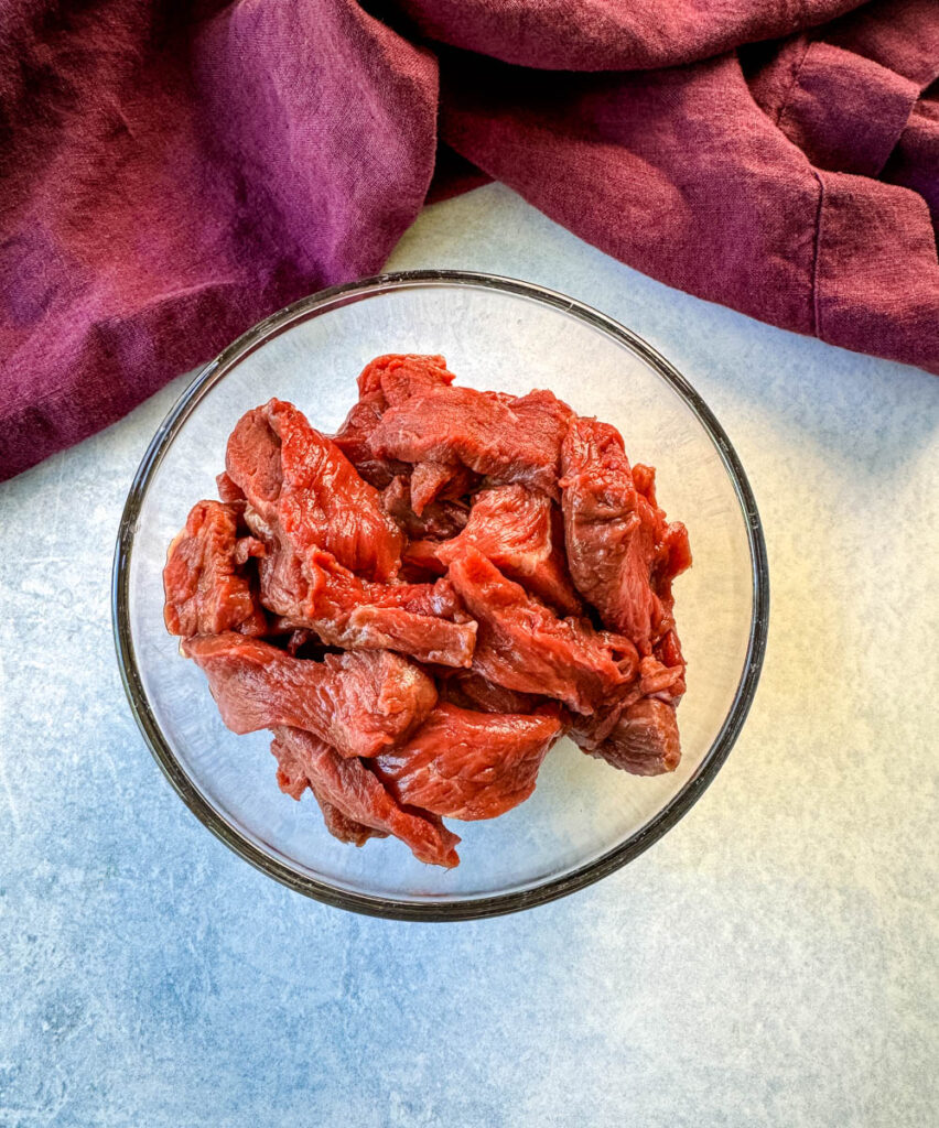 raw steak sliced into strips in a glass bowl