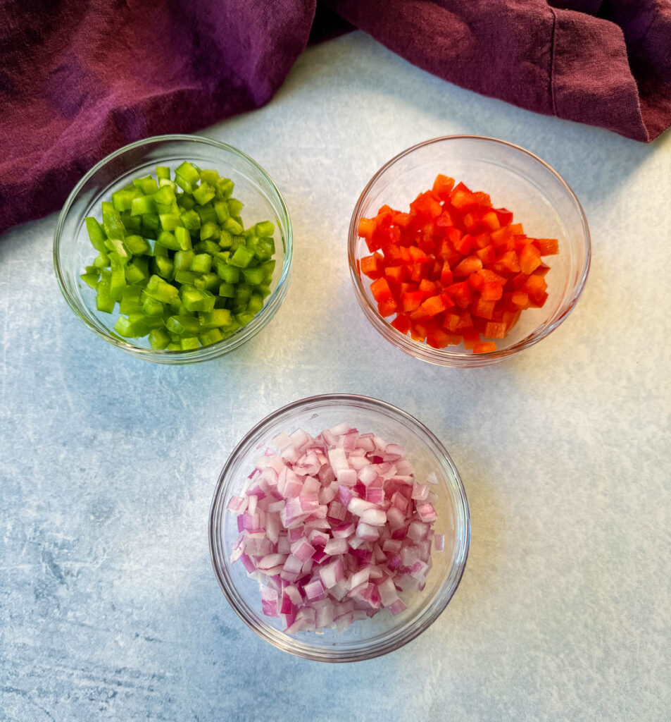 green and red bell peppers and red onions in separate glass bowls