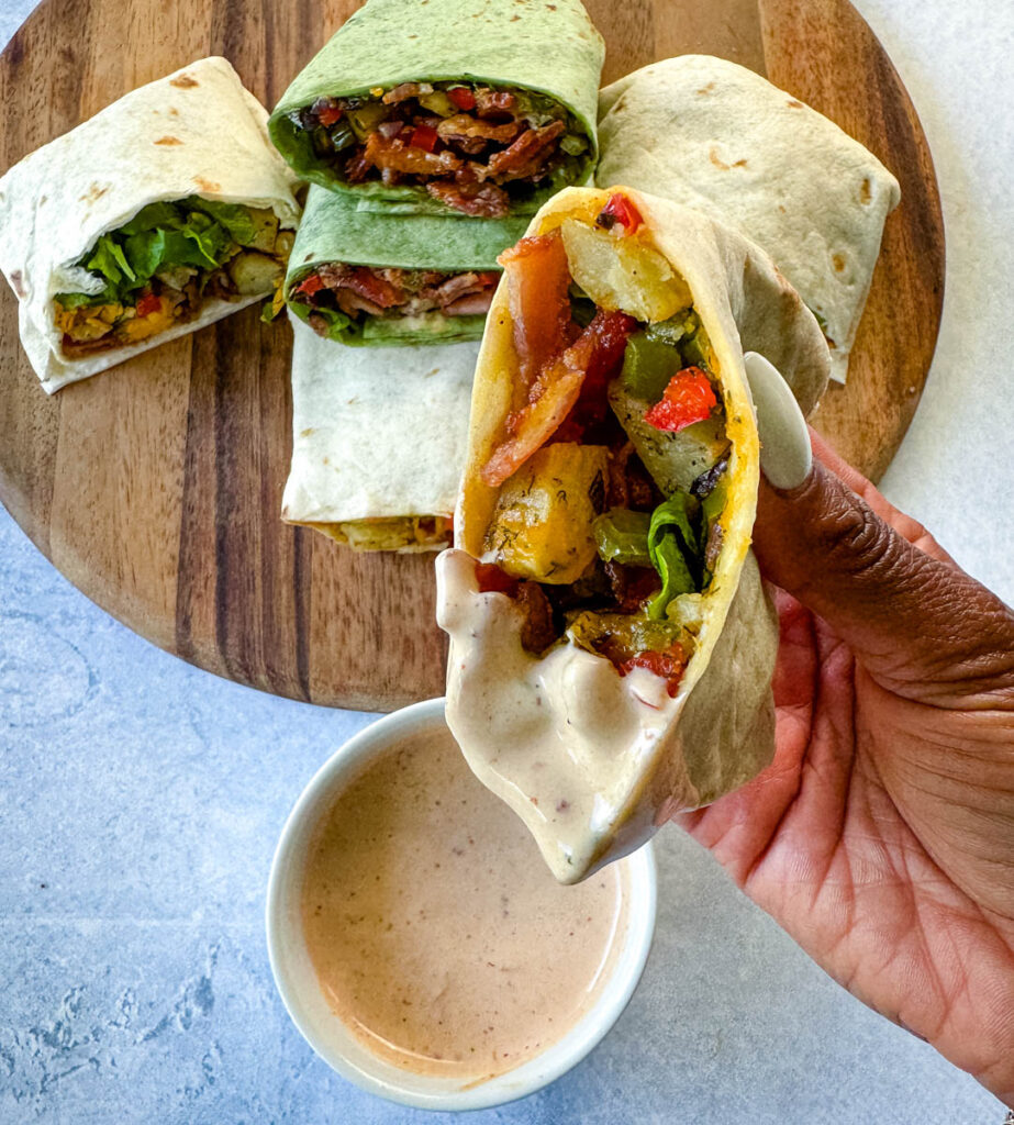 person holding breakfast burrito with bacon, potatoes, bell peppers and cheese