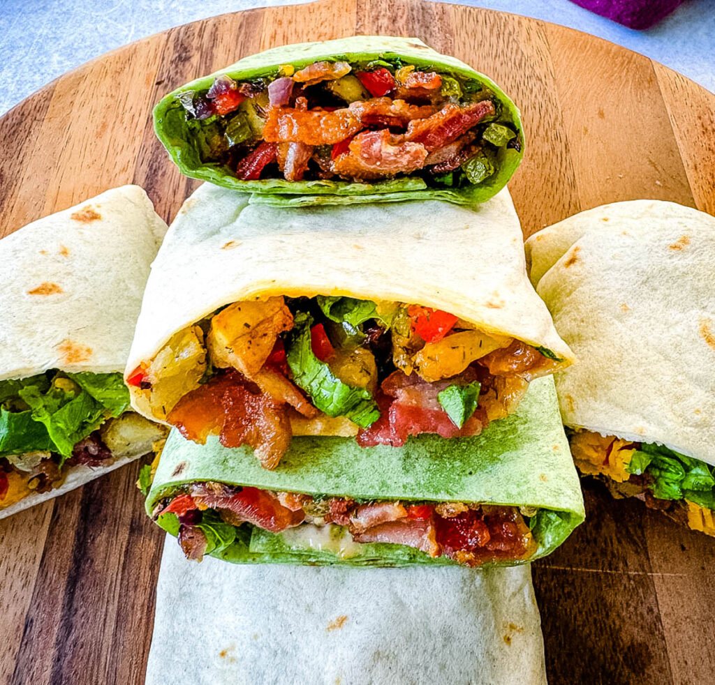 breakfast burritos with bacon, potatoes, bell peppers and cheese on a flat surface