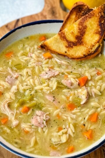 chicken orzo soup in a white bowl with toasted bread