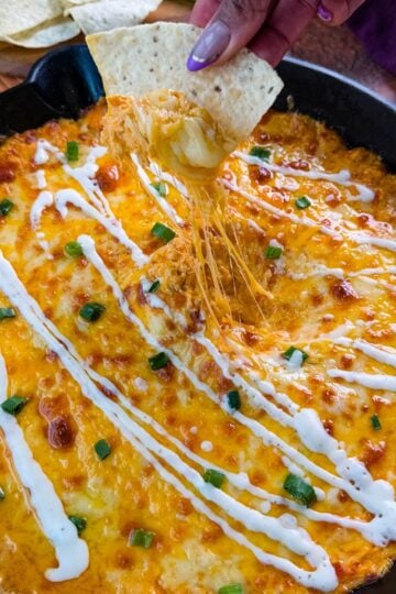Hot and cheesy Buffalo Chicken Dip in a black cast-iron skillet, garnished with fresh green onions and a drizzle of ranch dressing, ready to be served.