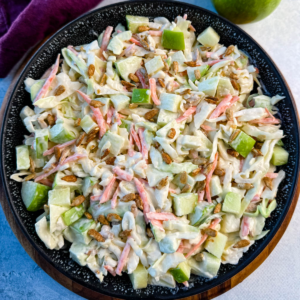 Overhead angle of a black speckled bowl filled with creamy apple coleslaw and sprinkled with sunflower seeds.
