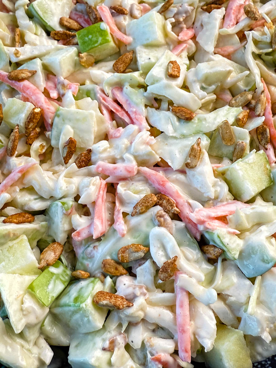 Close-up of creamy apple coleslaw topped with toasted sunflower seeds, showing chopped green apples, shredded cabbage, and carrots in a creamy dressing.