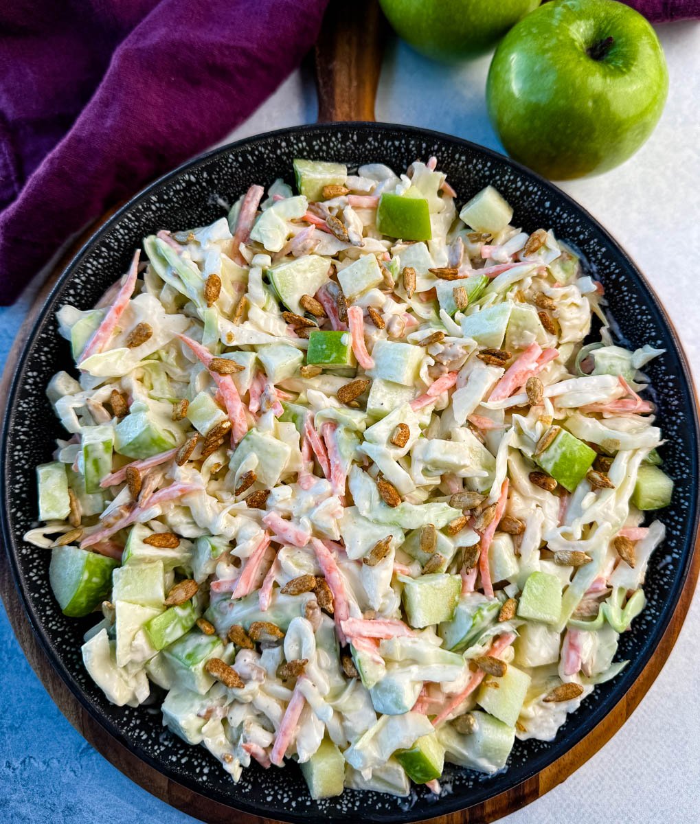 Overhead angle of a black speckled bowl filled with creamy apple coleslaw and sprinkled with sunflower seeds.