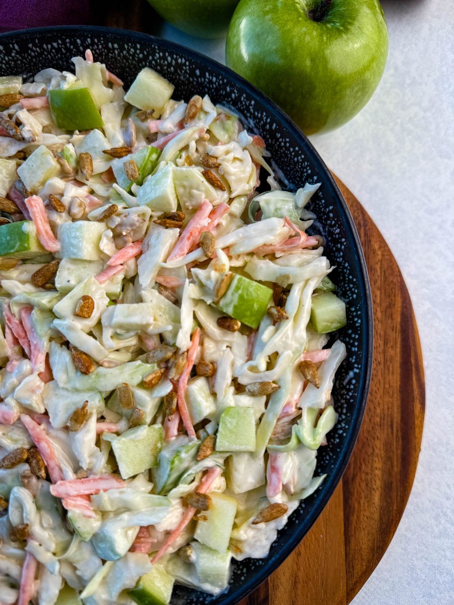 Overhead angle of a black speckled bowl filled with creamy apple coleslaw and sprinkled with sunflower seeds.