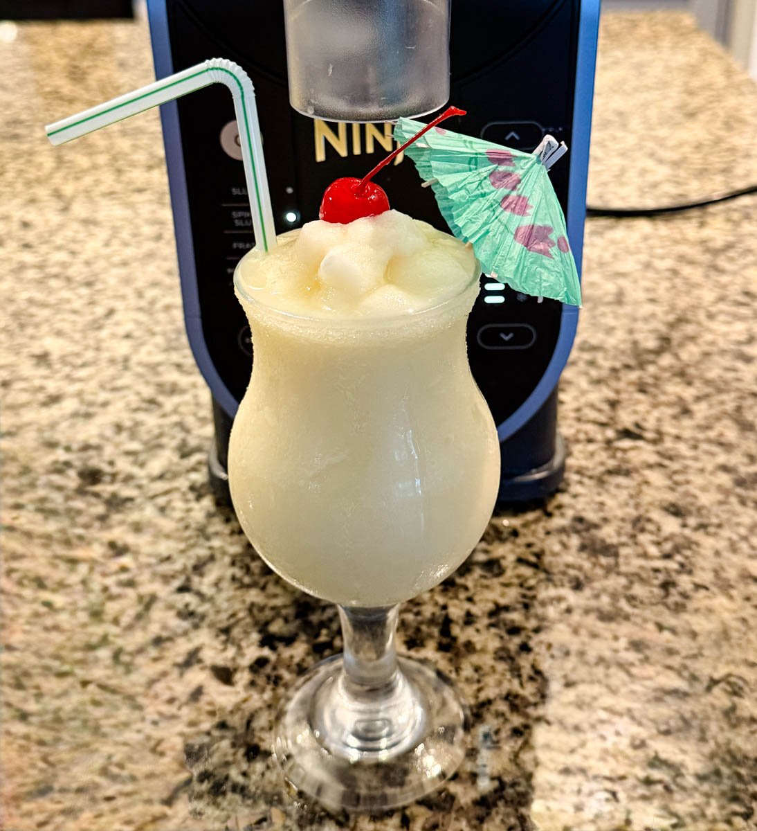 Finished piña colada dispensed into a glass directly from the Ninja Slushi machine, garnished with cherry and umbrella.