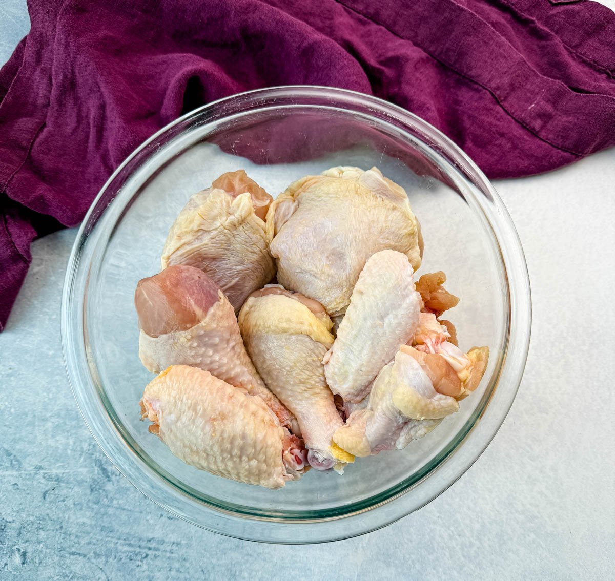 Raw chicken pieces, including drumsticks, wings, and thighs, placed in a large clear glass bowl, ready to be seasoned and breaded.