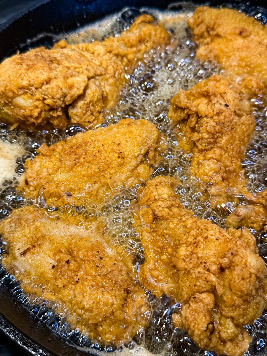 Fried chicken sizzling in a cast iron skillet filled with bubbling hot oil. The breading is crisping up to a deep golden color.