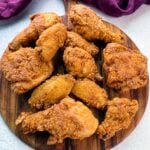 A wooden board topped with a spread of freshly fried, crispy chicken drumsticks, thighs, and wings, showcasing golden brown, crunchy coating.
