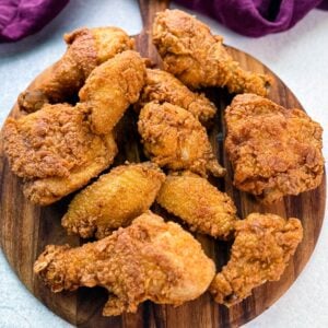 A wooden board topped with a spread of freshly fried, crispy chicken drumsticks, thighs, and wings, showcasing golden brown, crunchy coating.